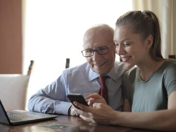 Kobieta pokazuje seniorowi obsługę telefonu