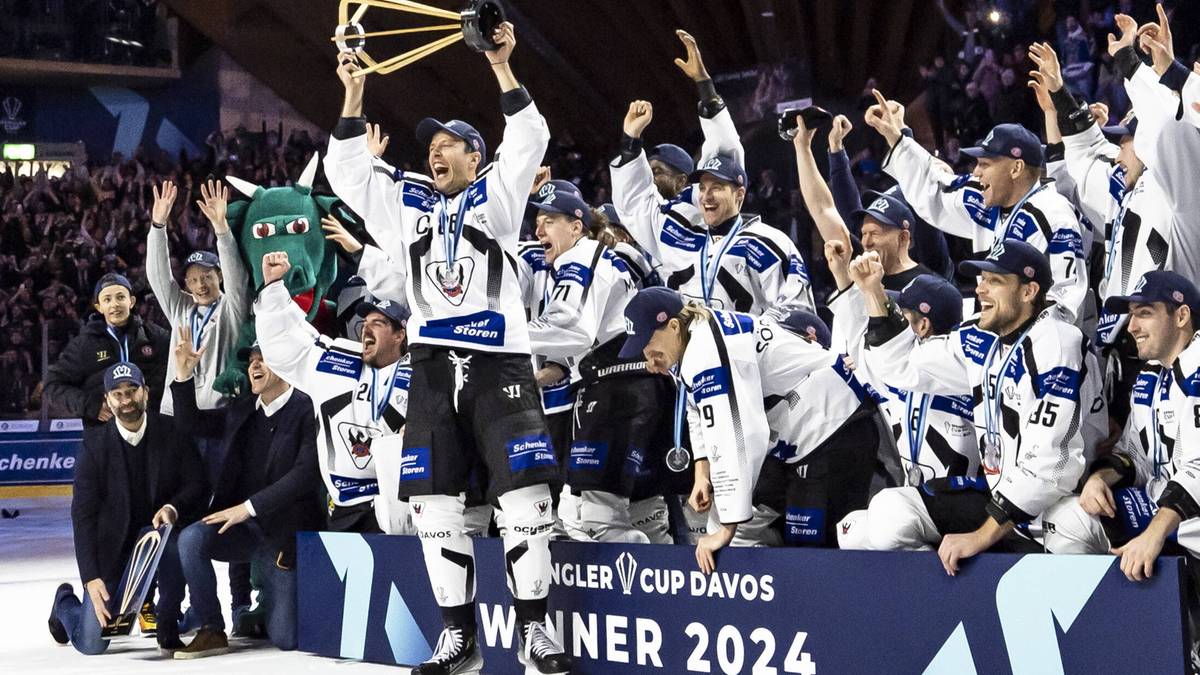 Drużyna hokejowa w niebiesko-białych strojach świętuje zdobycie trofeum Pucharu Spenglera, unosząc je nad głowami.