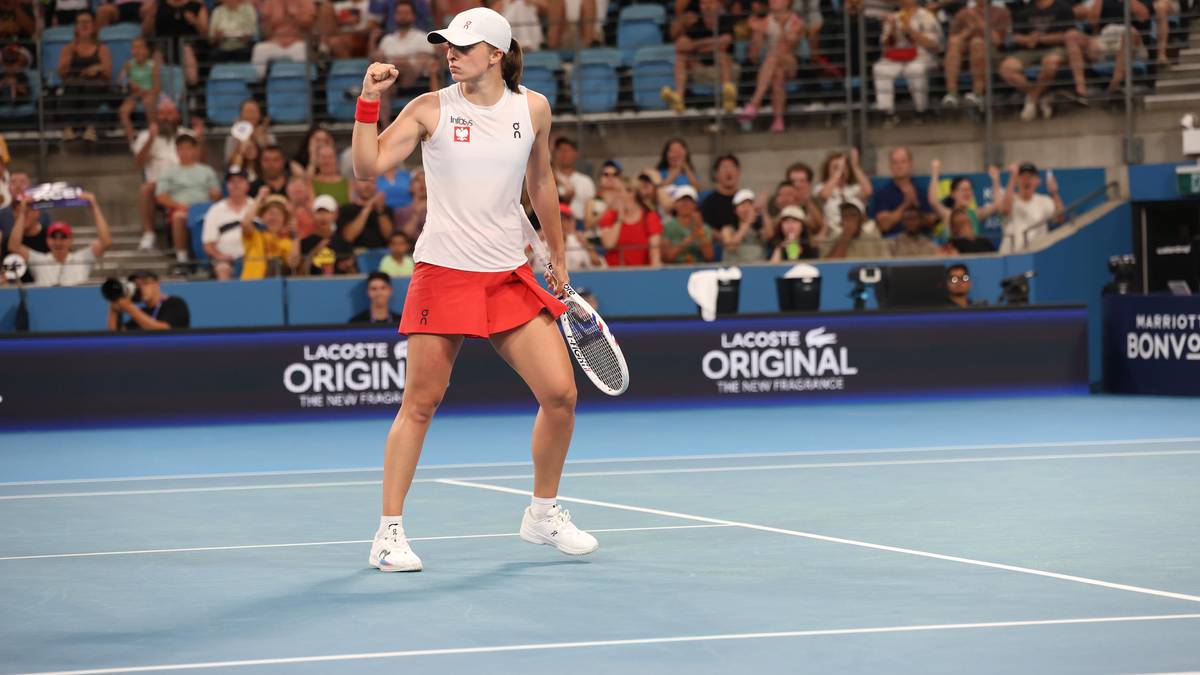 Tenisistka w stroju sportowym świętuje na korcie tenisowym, w tle publiczność i bandy reklamowe.