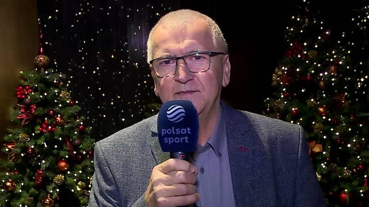 Mężczyzna w okularach i marynarce trzyma mikrofon z logo Polsat Sport na tle choinek ozdobionych lampkami.