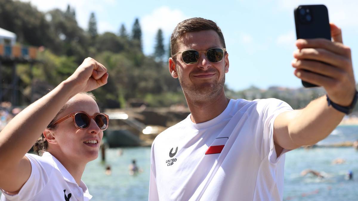 Mężczyzna i kobieta robią sobie selfie na tle plaży, oboje są uśmiechnięci.