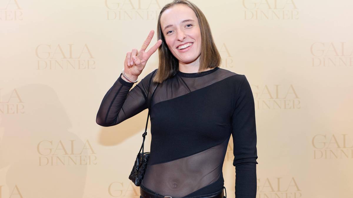 Iga Świątek pokazuje znak "V" palcami, uśmiechając się.