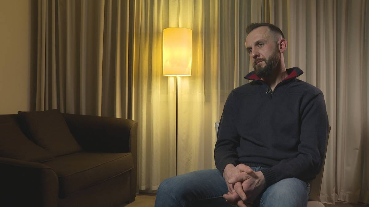 Mężczyzna siedzi na krześle, zamyślony, w tle kanapa i lampa