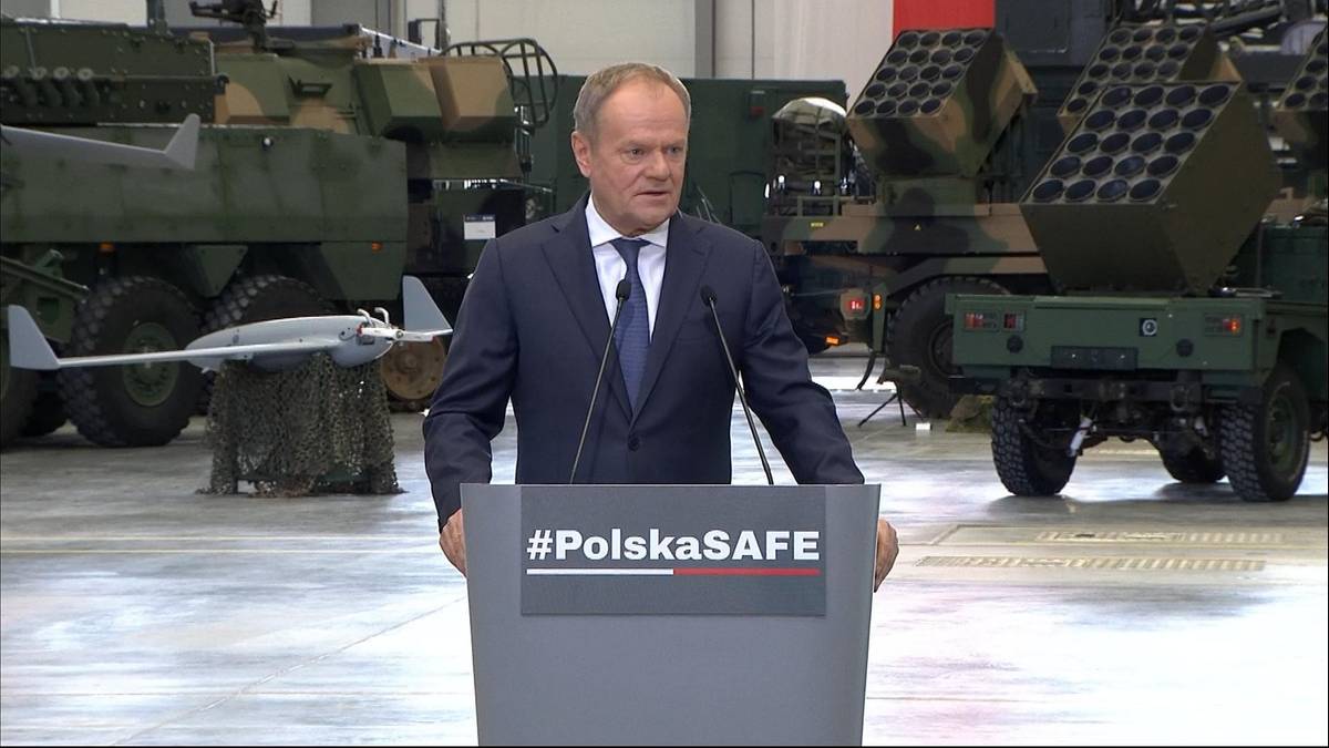 Każda chwila jest ważna. Szef rządu bez ogródek o "trzech fałszach". 3 Premier Donald Tusk przemawia przy mównicy z napisem "#PolskaSAFE", w tle widoczne wozy bojowe i dron.