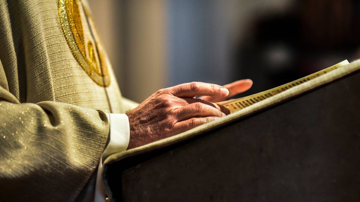 Zbliżenie na dłoń duchownego spoczywającą na otwartej księdze.