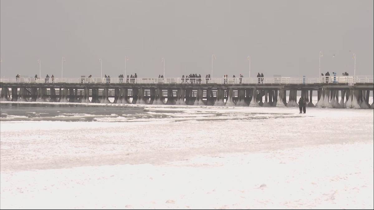 Zamarznięty Bałtyk z widocznym molo w tle, po lodzie spaceruje para.