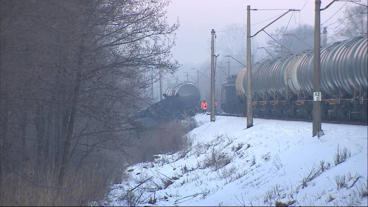 Wykolejony pociąg towarowy złożony z cystern przewożących olej napędowy, stojący na zasypanych śniegiem torach kolejowych.