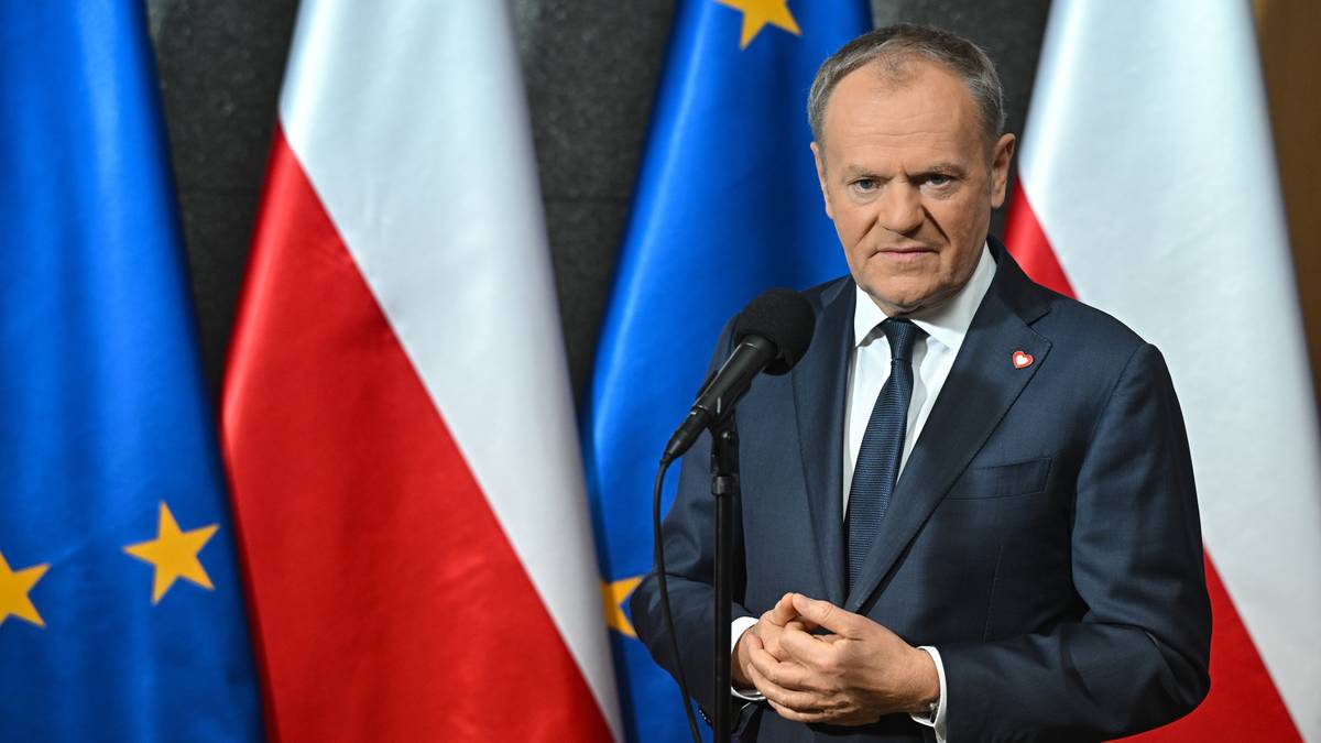 Premier Donald Tusk stoi przed polskimi i unijnymi flagami.