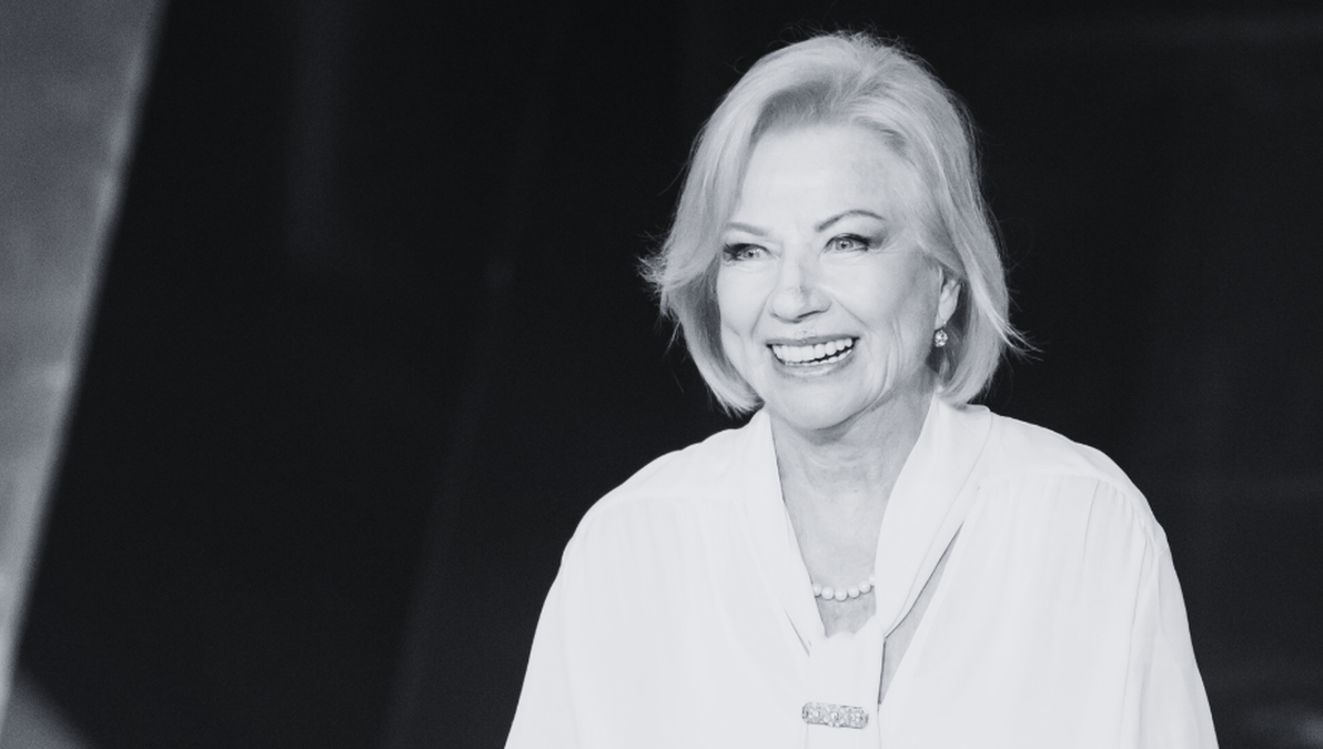 Uśmiechnięta starsza kobieta w jasnej bluzce i naszyjniku.