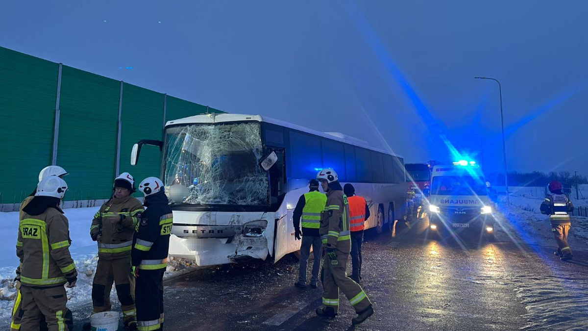 Miejsce wypadku z udziałem dw&oacute;ch autokar&oacute;w, widoczni ratownicy straży pożarnej i uszkodzone pojazdy na tle zimowego krajobrazu.