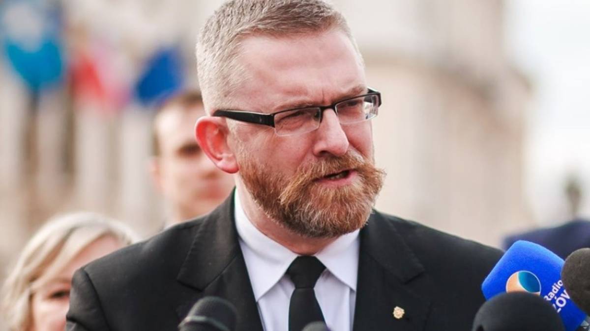 Mężczyzna w garniturze z okularami i brodą, m&oacute;wiący do mikrofonu.