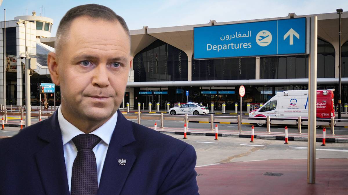 Karol Nawrocki, prezydent, w garniturze z krawatem, stoi na tle lotniska z tablicą "Departures".