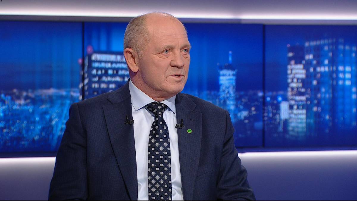 Mężczyzna w garniturze i krawacie przemawia w studiu telewizyjnym, w tle widać nocną panoramę miasta.