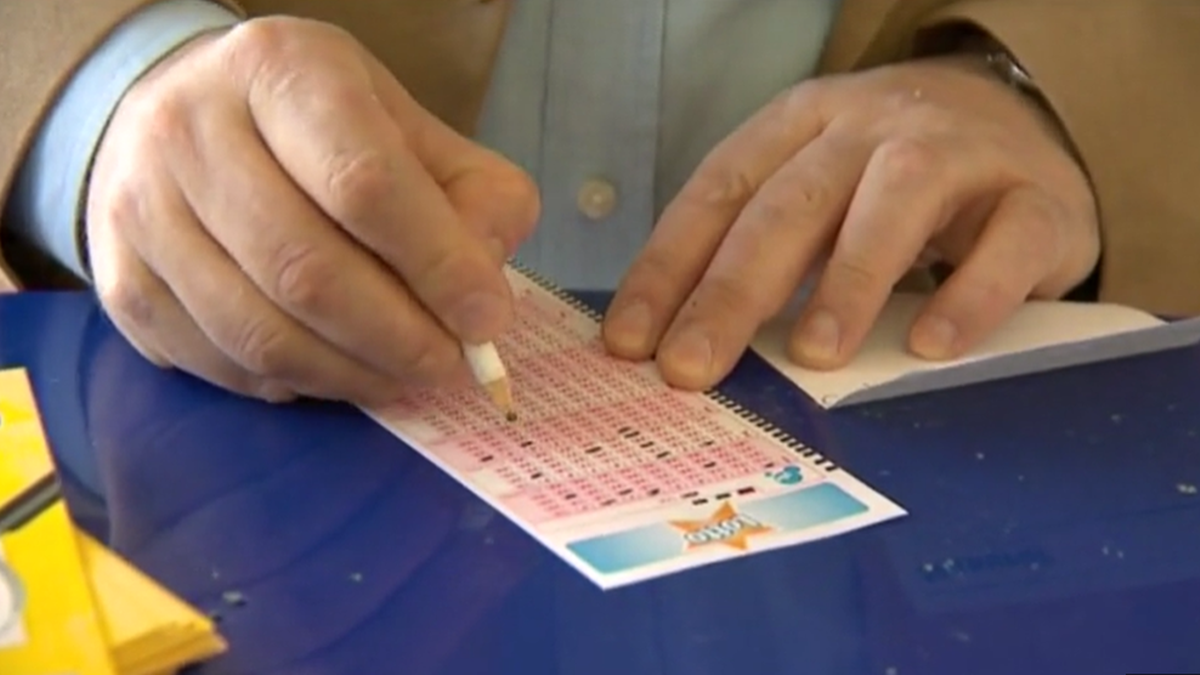 Dłoń gracza zaznacza liczby na kuponie Lotto oł&oacute;wkiem.