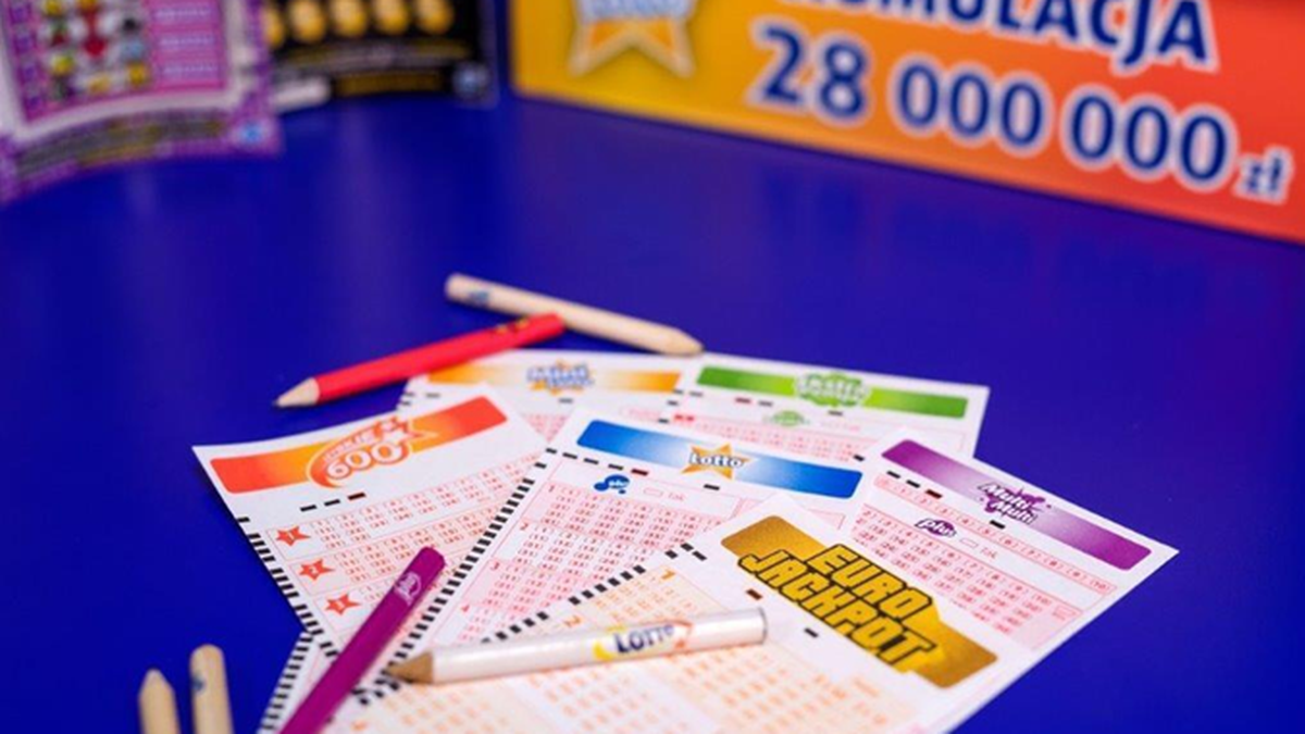 Lotto: Wyniki losowania z 28.03.2026. Odkryj wylosowane numery. 3 Kilka kuponów lotto i zdrapek leżących na niebieskim stole, wśród nich kupon "Eurojackpot". W tle plansza z informacją o kumulacji 28 milionów złotych. Obok kuponów znajdują się kolorowe kredki.