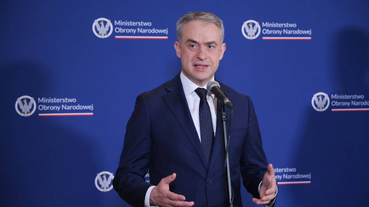 Minister cyfryzacji Krzysztof Gawkowski przemawia do mikrofonu na tle niebieskiej ściany z logo Ministerstwa Obrony Narodowej.