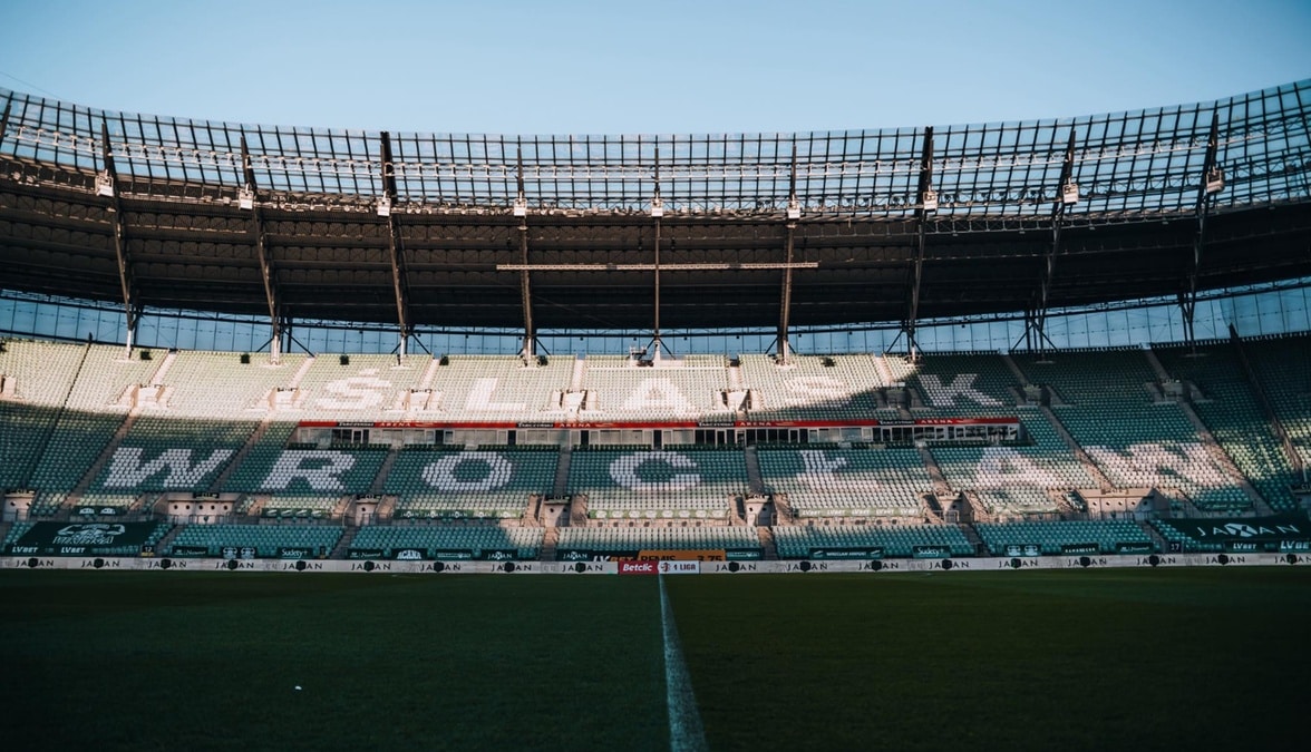 Widok na trybuny stadionu z napisem "ŚLĄSK WROCŁAW" widocznym na zielonych siedzeniach oraz na murawę boiska.