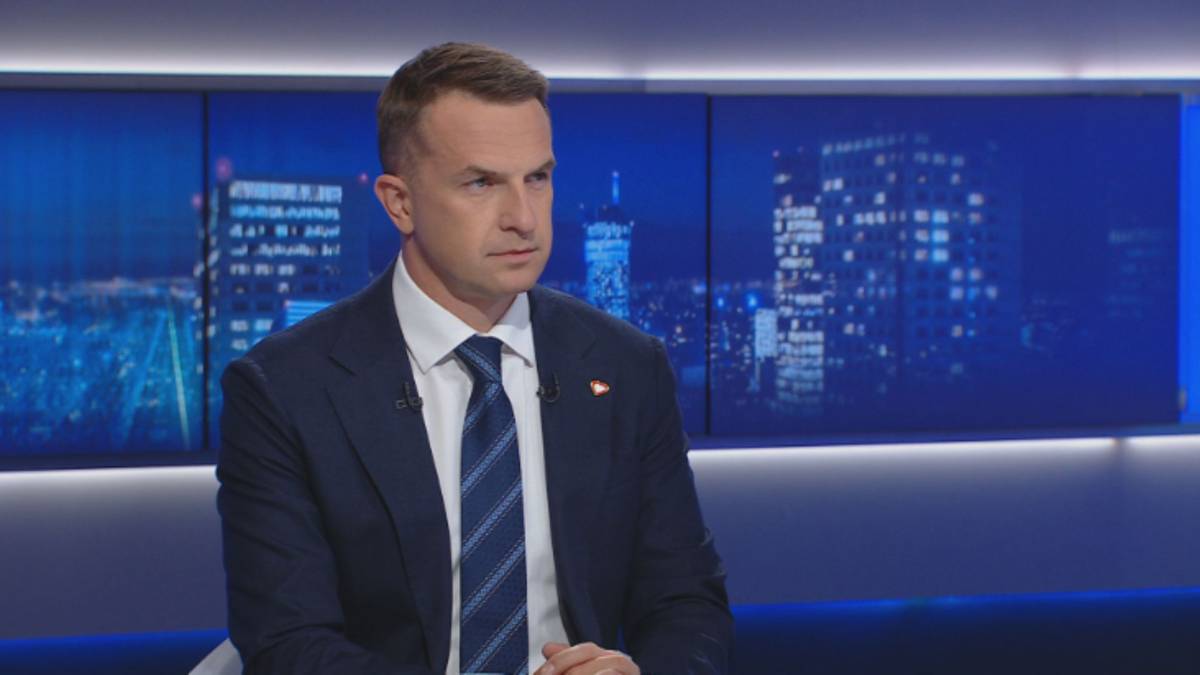 Mężczyzna w garniturze i krawacie siedzi w studio telewizyjnym.