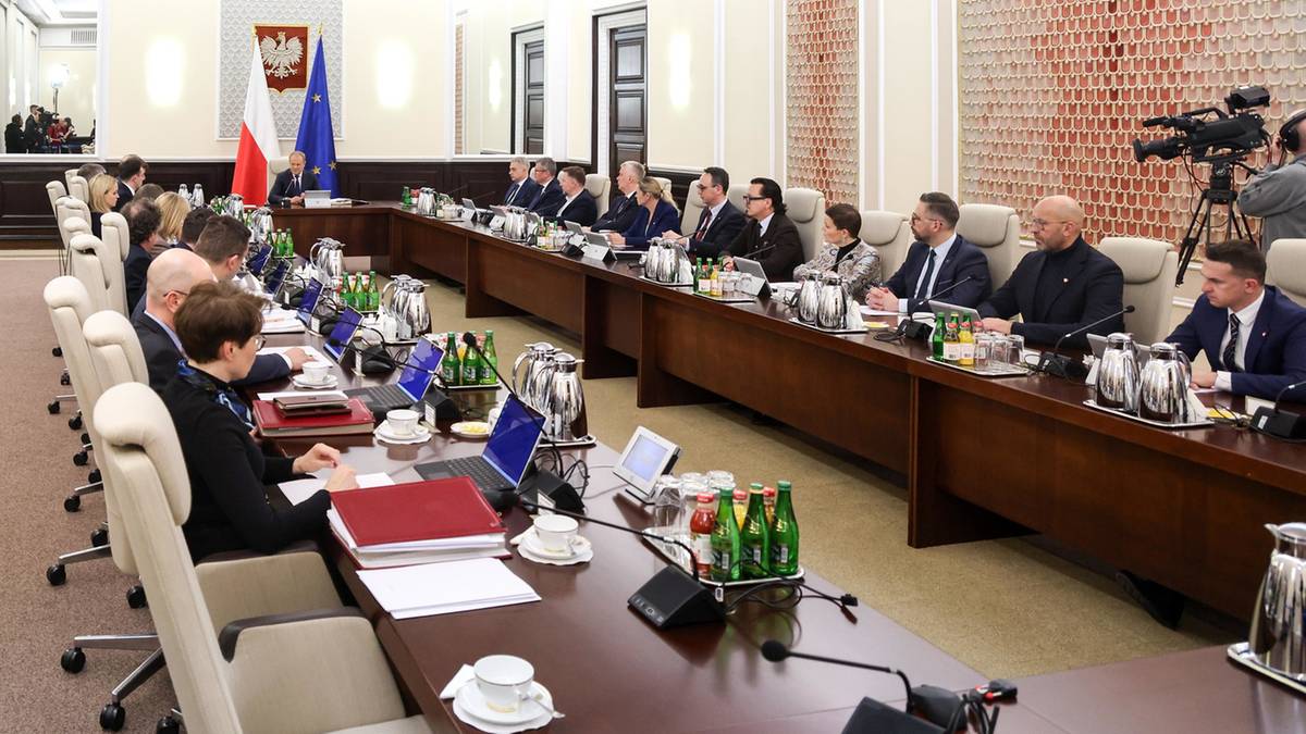 Uczestnicy posiedzenia siedzą przy długim stole w sali konferencyjnej, podczas gdy jedna osoba przemawia.