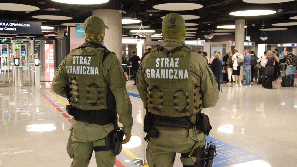 Dw&oacute;ch funkcjonariuszy Straży Granicznej w mundurach patrzy w stronę terminala lotniska.