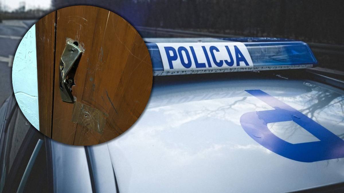 Zbliżenie na uszkodzoną klamkę drewnianych drzwi oraz fragment dachu radiowozu policyjnego z napisem POLICJA.