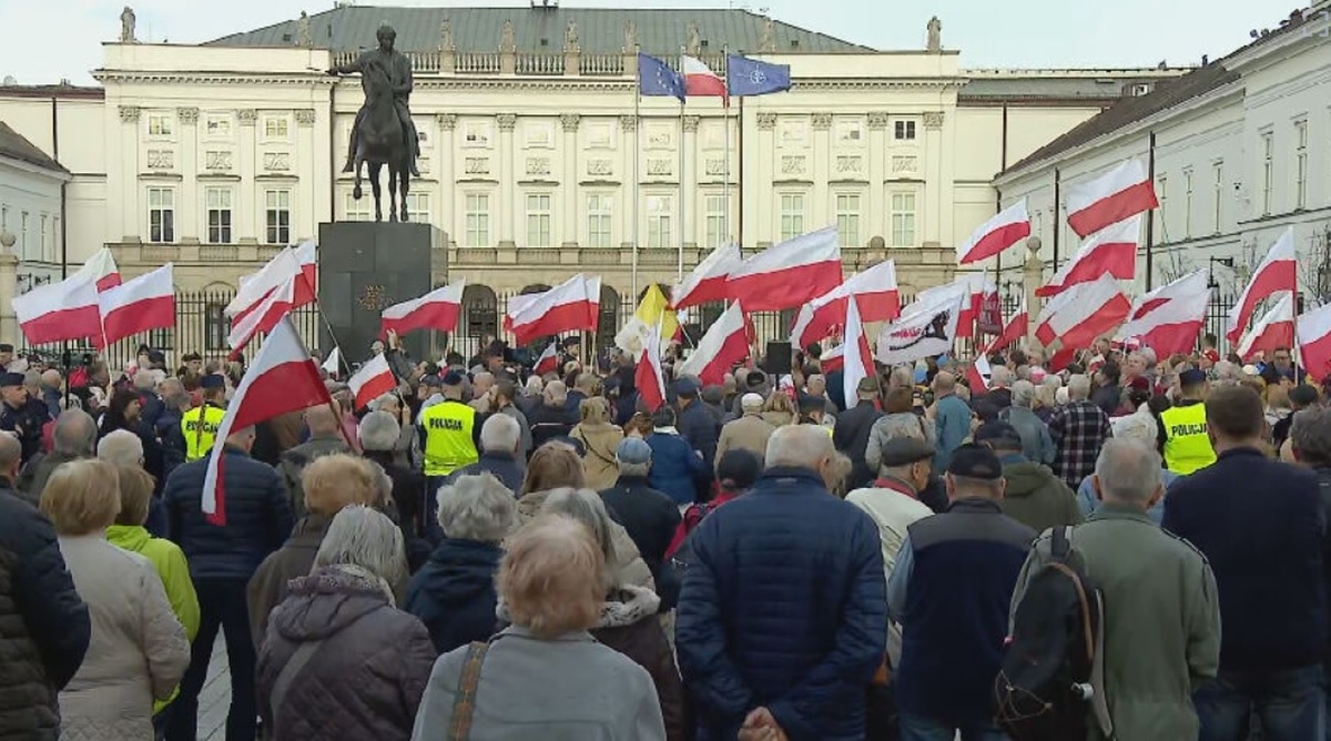 Tłum ludzi trzymających polskie flagi na placu przed Pałacem Prezydenckim w Warszawie. W tle widoczny pomnik konny.