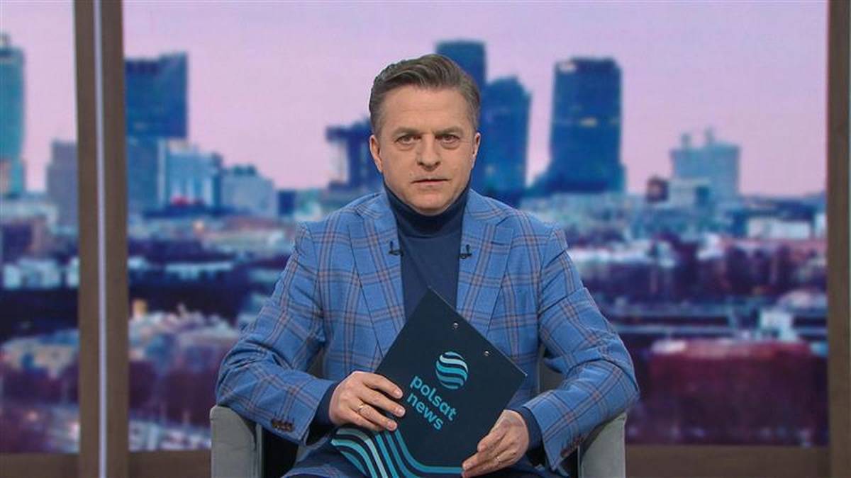 Bogdan Rymanowski siedzi w studiu telewizyjnym, trzymając tablet z logo Polsat News.