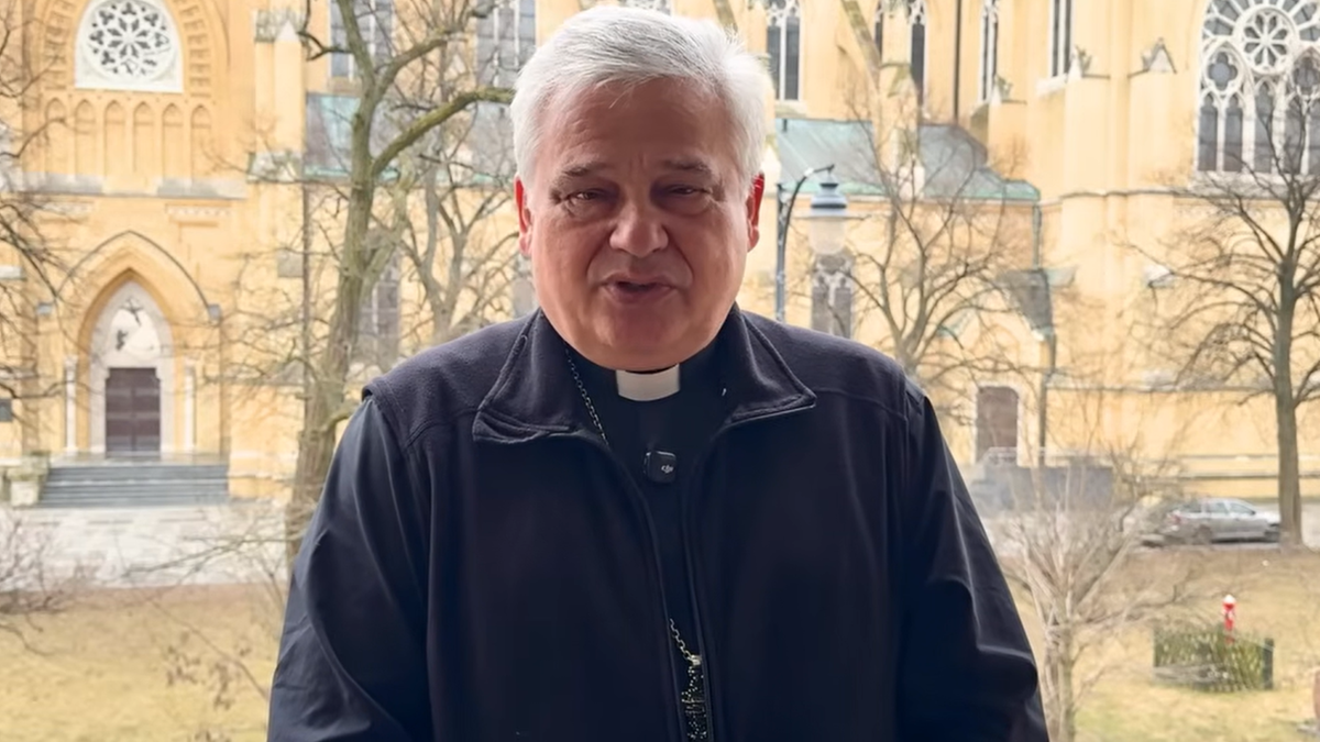 Kardynał Konrad Krajewski w sutannie i czarnej kurtce, stojący przed budynkiem ł&oacute;dzkiej archikatedry.