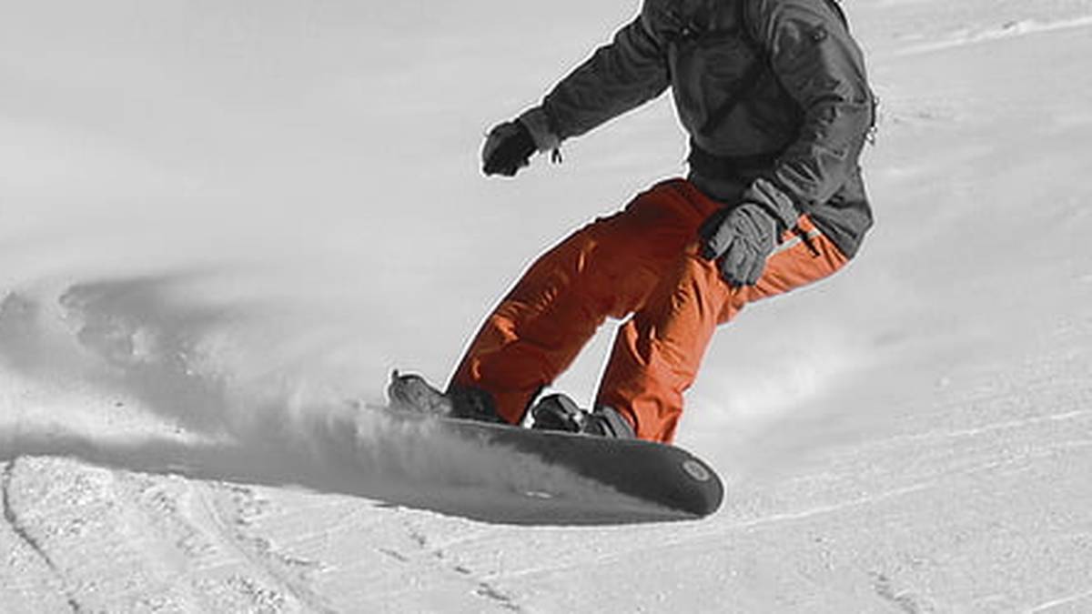 Osoba na snowboardzie zjeżdżająca ze stoku, tworząca obłok śniegu.