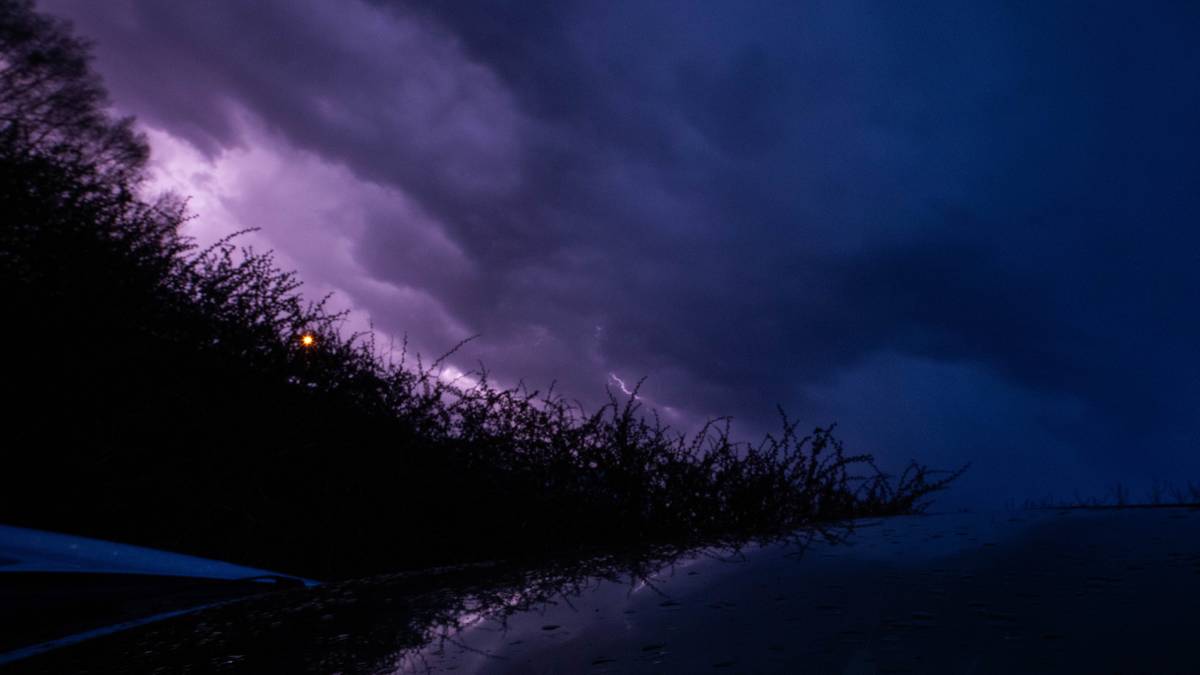 Czwartek: przelotne opady deszczu ze śniegiem. 3 Mroczne chmury burzowe z przebłyskami błyskawic nad ciemnym, wodnistym krajobrazem.