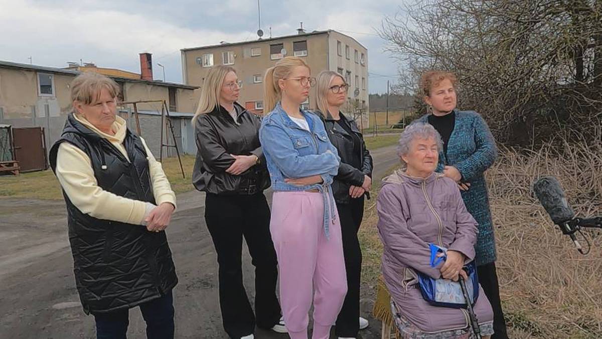 Grupa kobiet stoi na zewnątrz, przed budynkiem mieszkalnym, z mikrofonem w pobliżu.