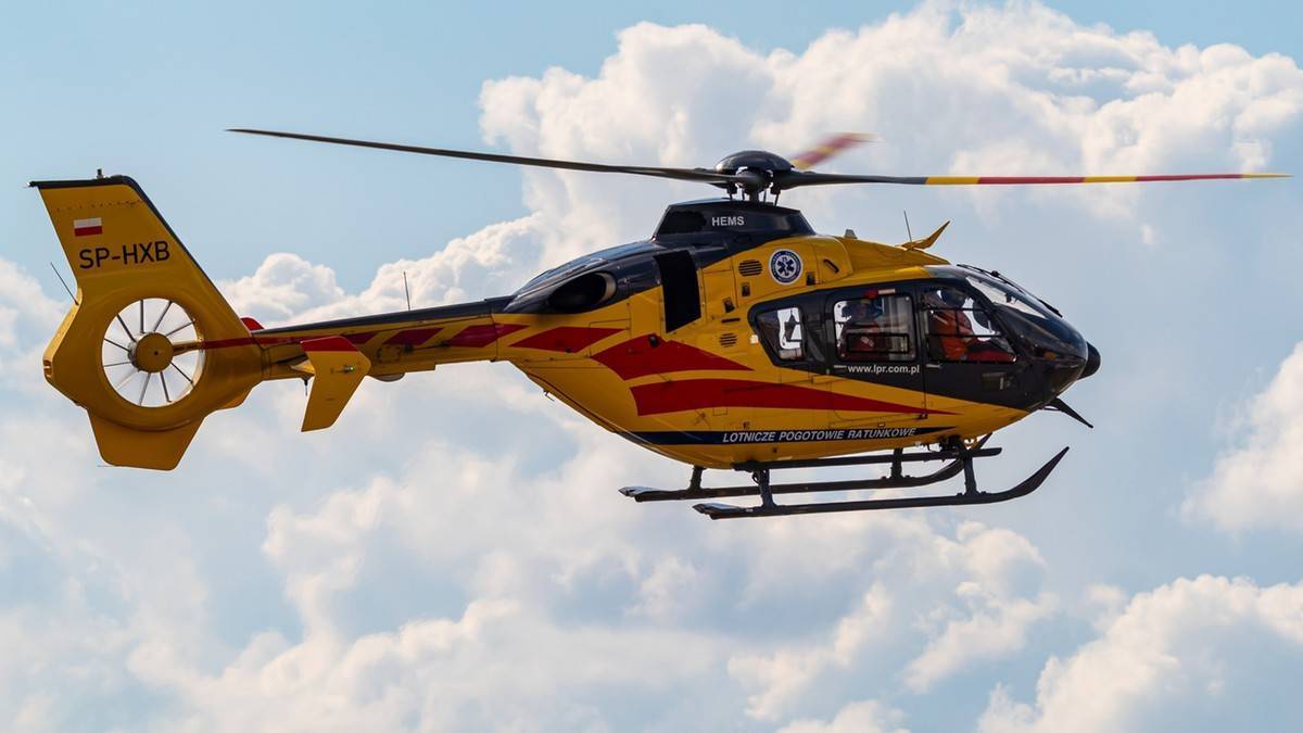 Tragedia w Wadowicach. Malec spadł z trzeciego piętra. 3 Żółty helikopter ratowniczy z czerwonymi pasami na tle błękitnego nieba z chmurami.