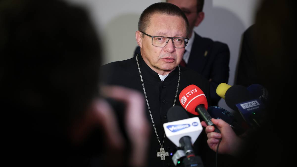 Kardynał Grzegorz Ryś w okularach i sutannie, otoczony przez mikrofony, wypowiada się do medi&oacute;w.