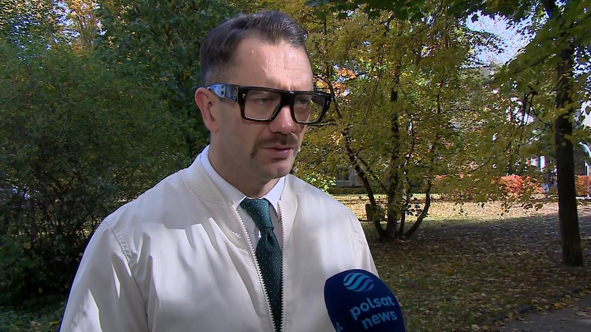 Poseł Łukasz Mejza w białej kurtce i ciemnym krawacie, ubrany w okulary w grubych oprawkach.