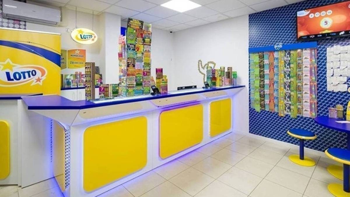 Lotto: Wyniki z 7 kwietnia. Zobacz wylosowane numery. 3 Widok wnętrza punktu sprzedaży gier liczbowych Lotto, z ladą sprzedażową, ekspozycją produktów i ekranem informacyjnym.