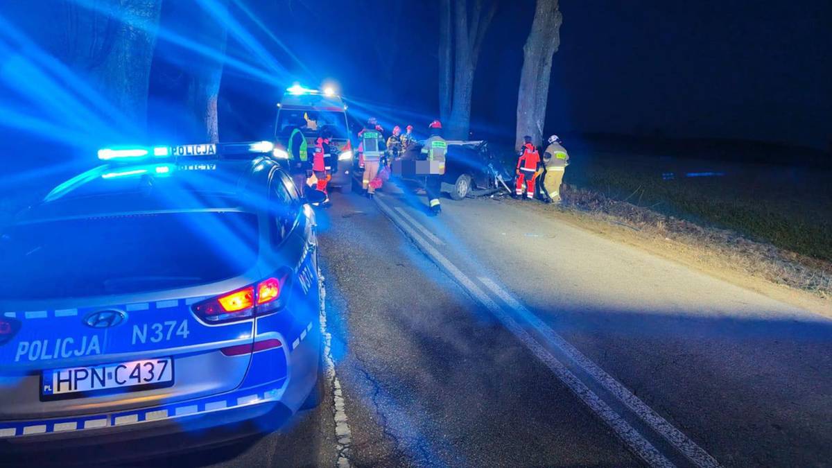 Tragiczne wypadki na Pomorzu. Dwóch kierujących poniosło śmierć. 3 Radiowóz policyjny z włączonymi niebieskimi sygnałami świetlnymi stoi na poboczu drogi, obok widoczni są ratownicy medyczni i inne pojazdy służb ratunkowych pracujące na miejscu wypadku.