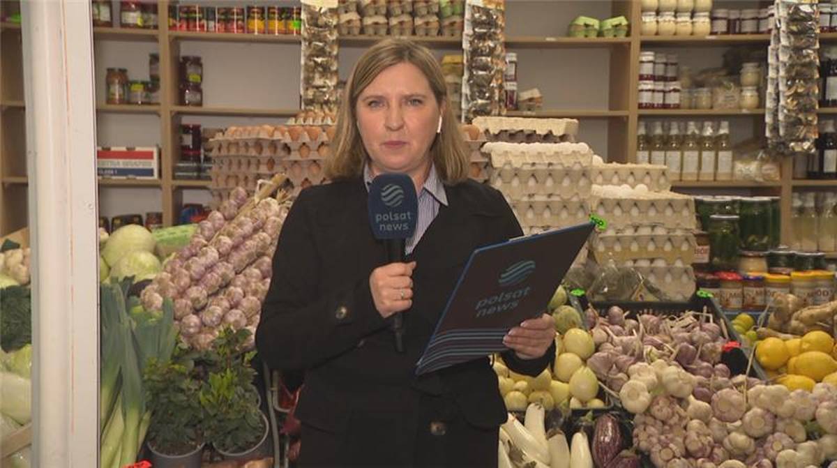 Co zyskało na cenie, a co stanieje? Wielkanocny koszyk – Polsat News. 4 Kobieta w czarnym stroju trzymająca mikrofon Polsat News i tablet, stoi przed stoiskiem z produktami spożywczymi.