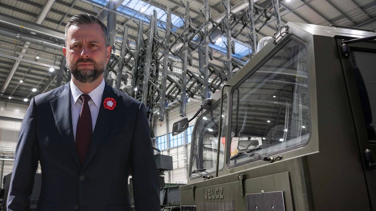 Minister Obrony Narodowej Władysław Kosiniak-Kamysz stoi obok sprzętu wojskowego w hali produkcyjnej.