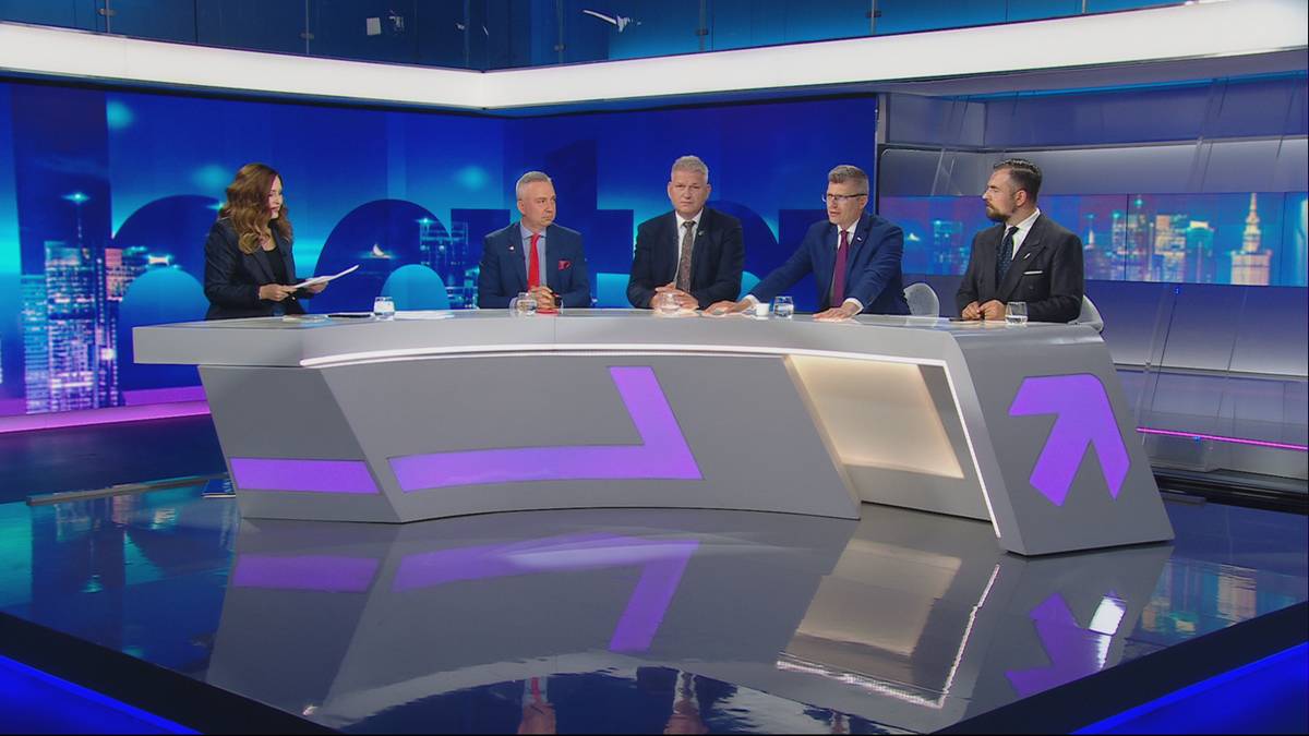 Pięć os&oacute;b siedzi przy futurystycznym stole w studiu telewizyjnym, na tle ekran&oacute;w wyświetlających miejskie panoramy.